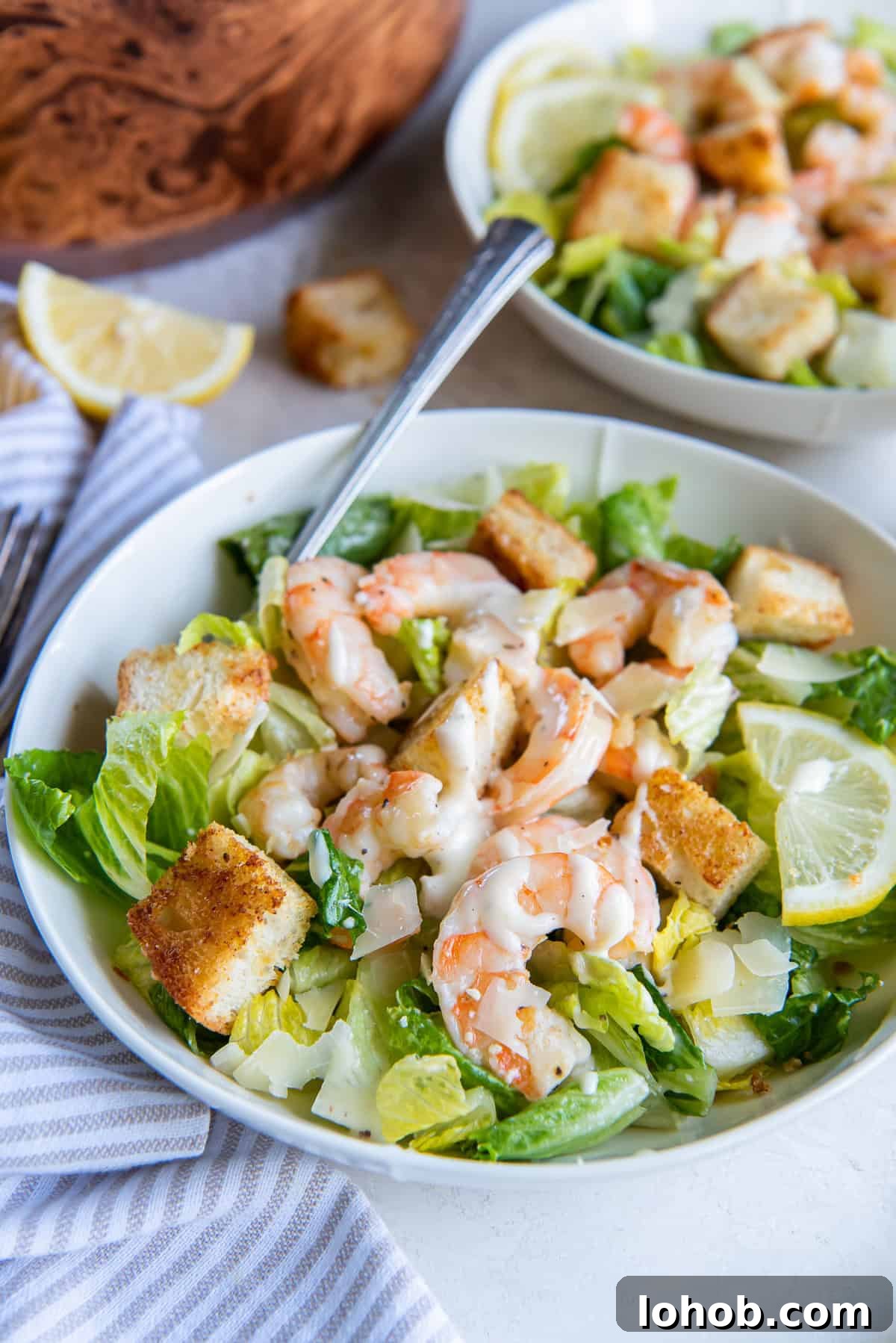 Grilled Shrimp Caesar Salad with Crispy Parmesan Croutons 13 A fork resting in a bowl with caesar salad with shrimp and, croutons, and dressing.