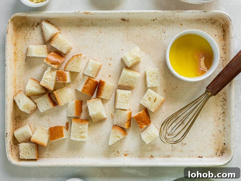 Grilled Shrimp Caesar Salad with Crispy Parmesan Croutons 6 Bread cubes on a baking sheet with a ramekin filled with melted butter and seasoning and a whisk.