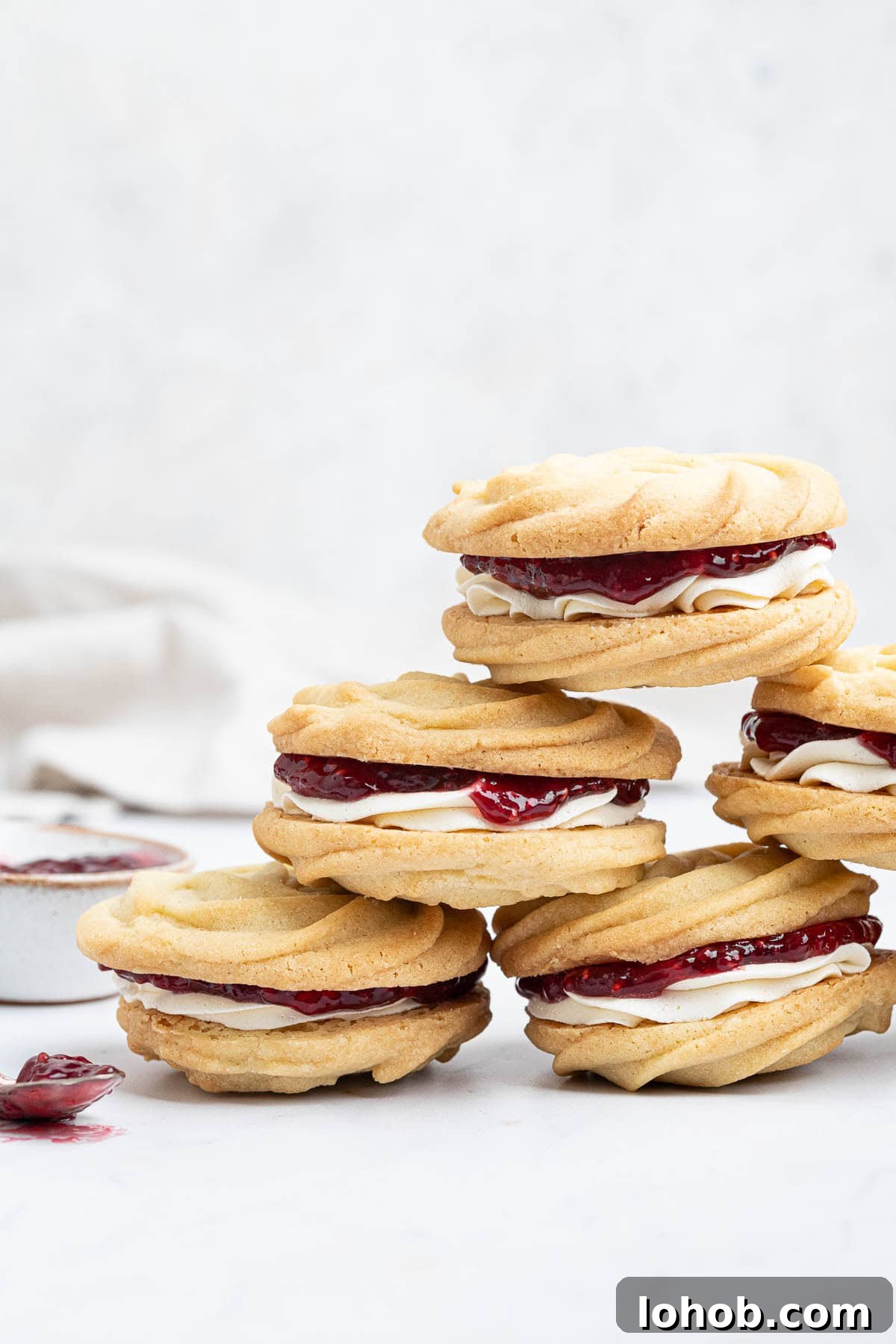 Vegan Viennese Whirls Recipe — Crisp, Buttery Cookies 12 A stack of vegan Viennese whirls with a bowl and spoon of jam.