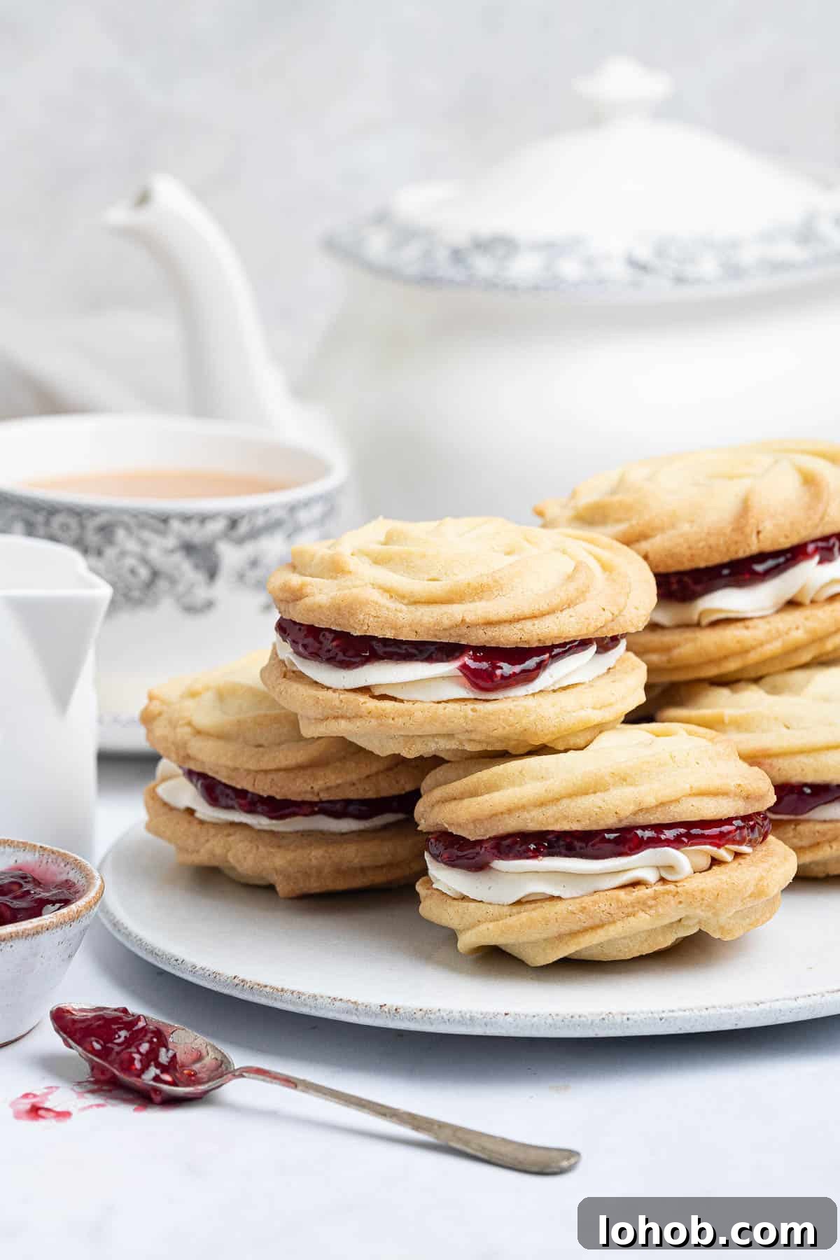 Vegan Viennese Whirls Recipe — Crisp, Buttery Cookies 4 Vegan Viennese whirls on a plate with a teapot, cup of tea and bowl of jam.