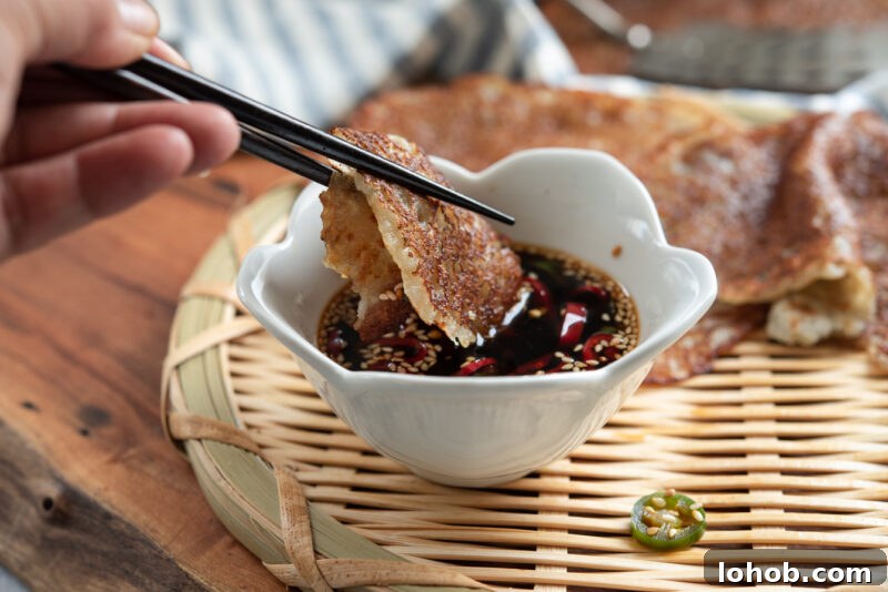 Chopsticks dipping crispy Korean potato pancake (gamja-jeon) into soy chili sauce
