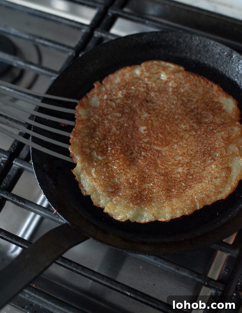A spatula flipping Korean potato pancake (gamja-jeon) to reveal its golden, crispy side