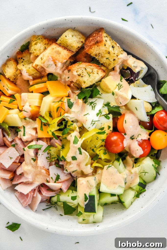 plated chef salad with fresh veggies, croutons, meat and cheese on a bed of romaine with dressing.