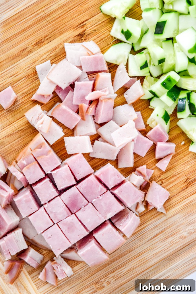 cutting up the ham and cucumber on a cutting board for the easy chef salad meal prep.