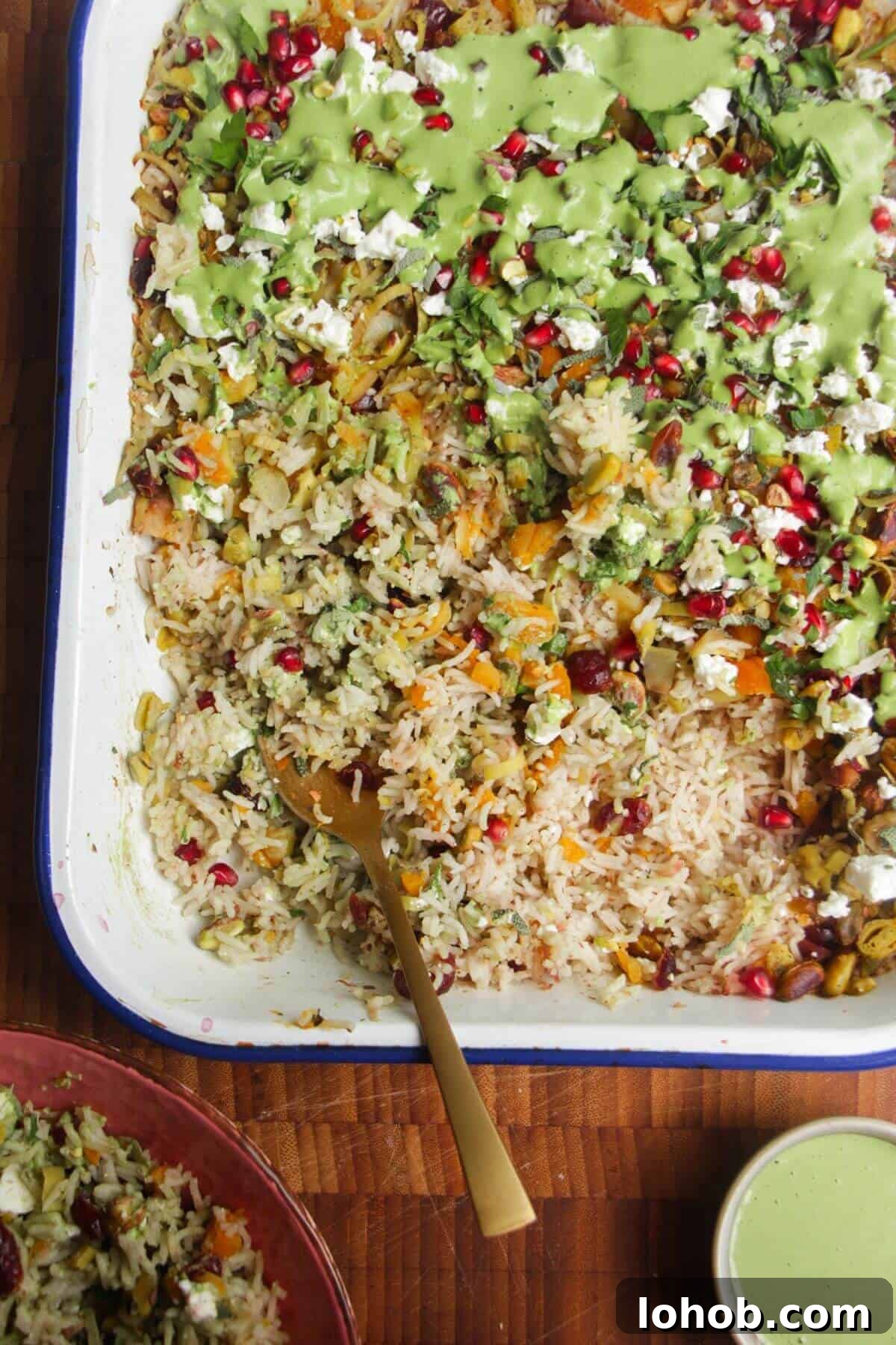 Spoon in baked rice topped with feta, pomegranate seeds and green tahini sauce.