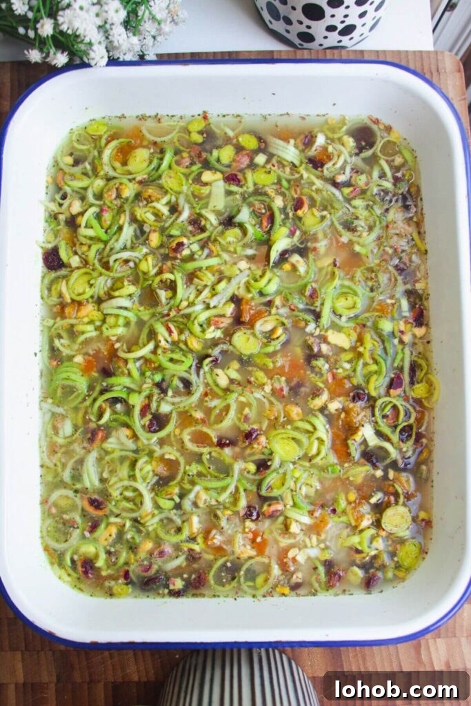 Rice, leeks, seasoning and stock in a large white oven dish.