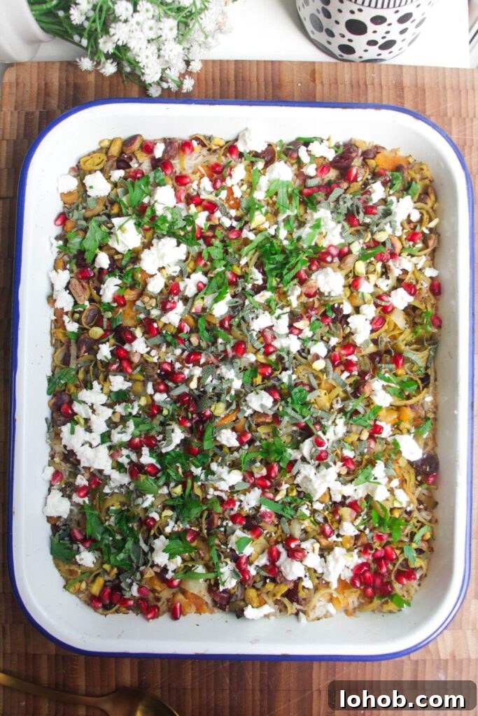 Baked rice topped with feta, pomegranate seeds and herbs in an oven dish.