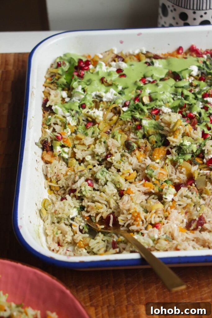 Spoon in baked rice topped with feta, pomegranate seeds and green tahini sauce.