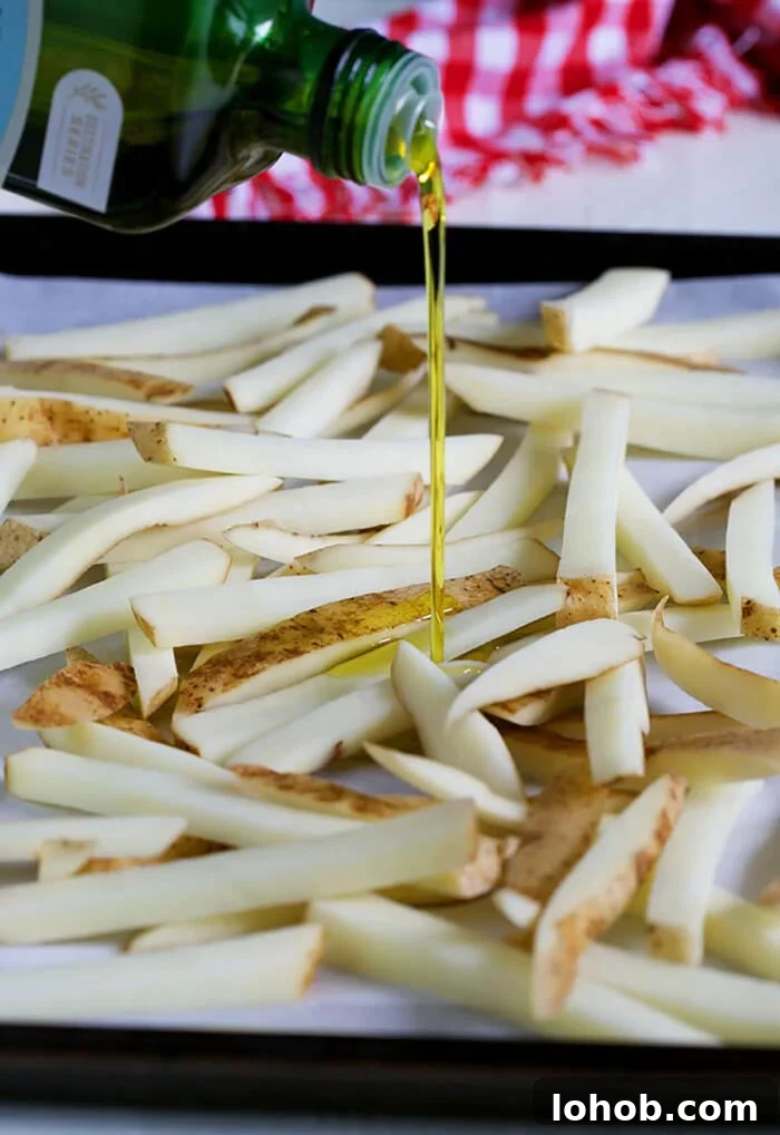 Crispy Parmesan Truffle Fries Recipe with Garlic and Herbs 6 olive oil being drizzled over potatoes on a baking sheet