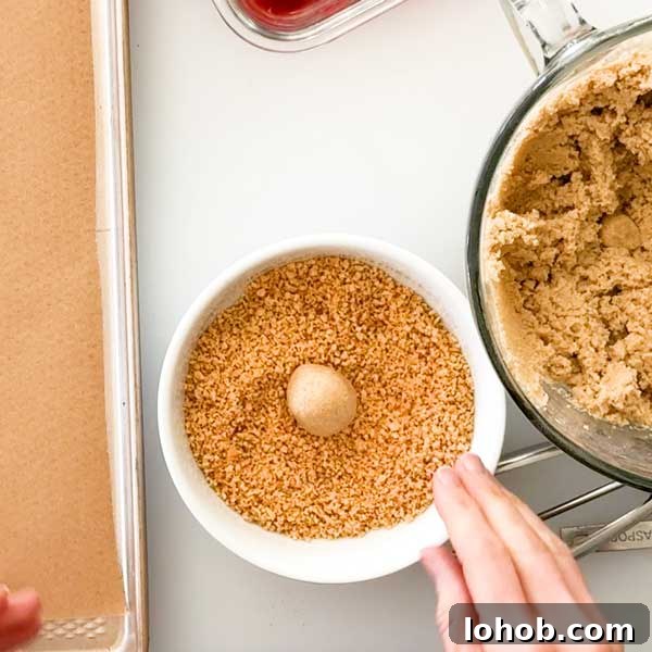 Gluten-Free Peanut Butter and Jelly Thumbprint Cookies 6 Rolling the peanut butter cookie dough ball in a bowl of crushed peanuts.