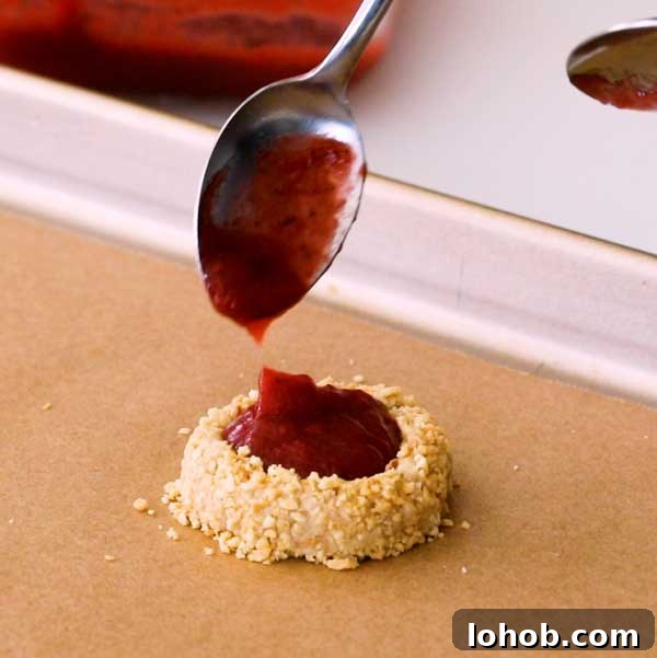 Gluten-Free Peanut Butter and Jelly Thumbprint Cookies 9 Dropping the strawberry jam into the center of the peanut butter cookie with a spoon.