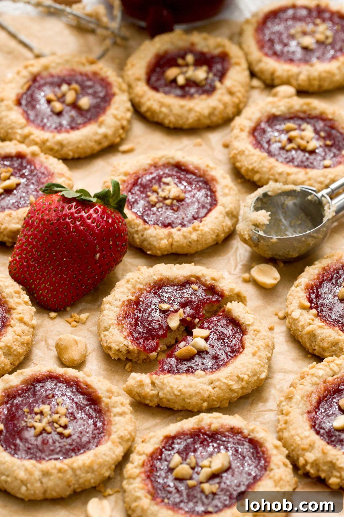 Gluten-Free Peanut Butter and Jelly Thumbprint Cookies 10 Peanut butter and jelly thumbprint cookies on a parchment paper with one cookie broken in half in the center.