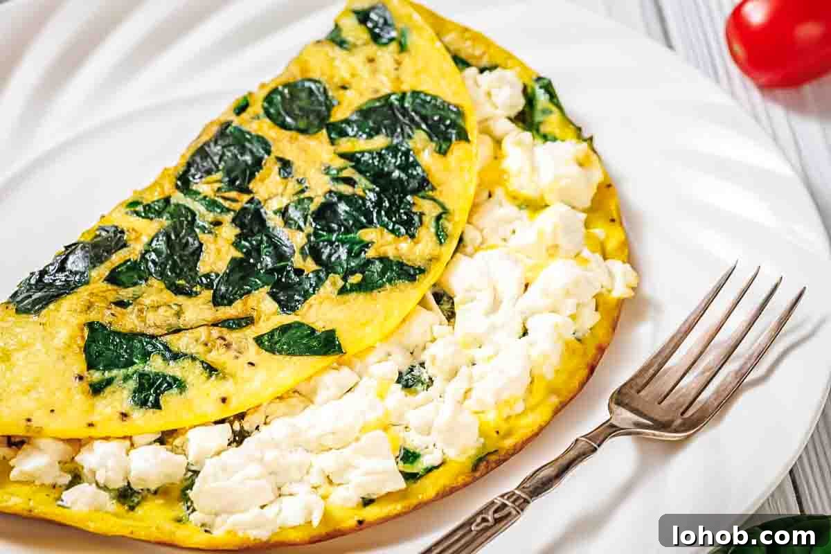 25 Morning Breakfast Ideas to Refresh Your Weekly Menu 2 A spinach and feta cheese omelette folded on a white plate with a fork beside it.