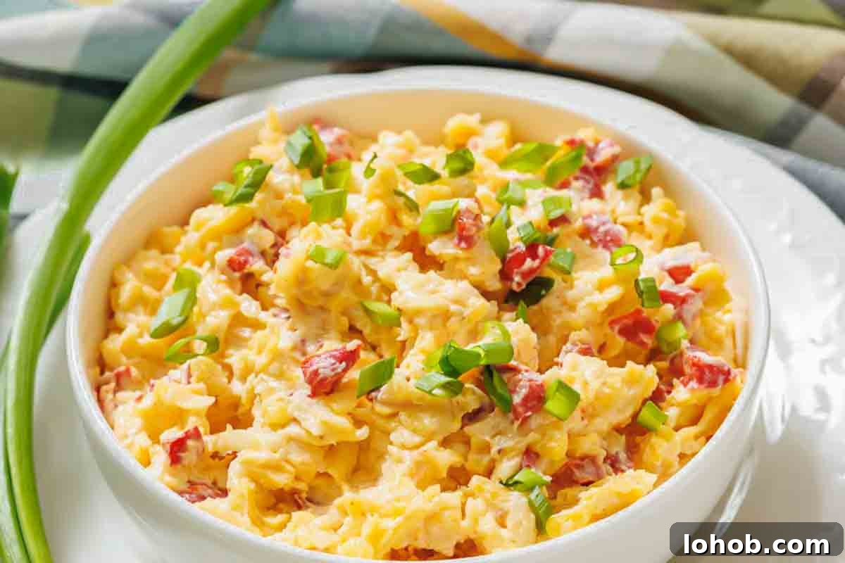 25 Morning Breakfast Ideas to Refresh Your Weekly Menu 17 A bowl of pimento cheese spread with diced red bell peppers and topped with chopped green onions, set on a white plate.