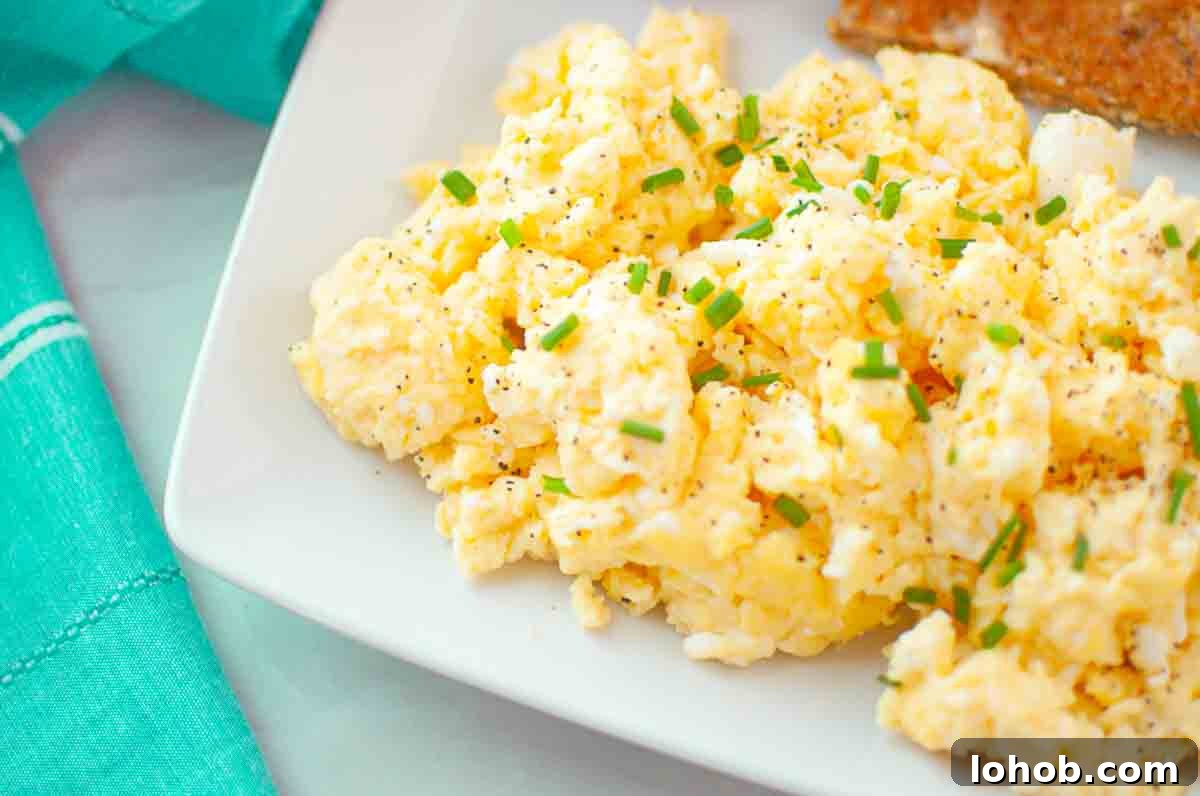 25 Morning Breakfast Ideas to Refresh Your Weekly Menu 20 Scrambled eggs garnished with chopped chives and black pepper, served on a white plate next to a piece of toast.