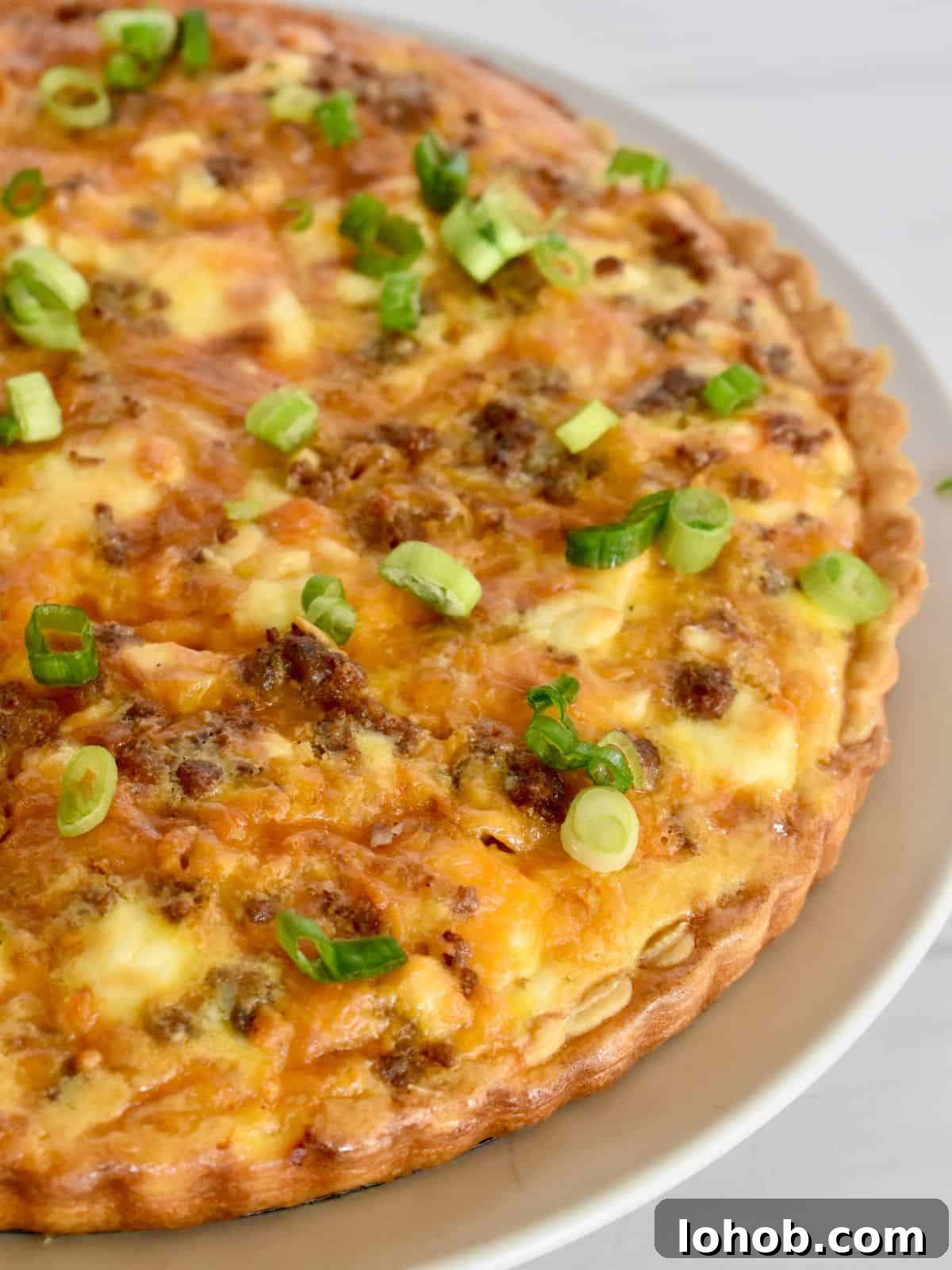 Breakfast tart with sausage and cheddar on a plate with green onion on top.