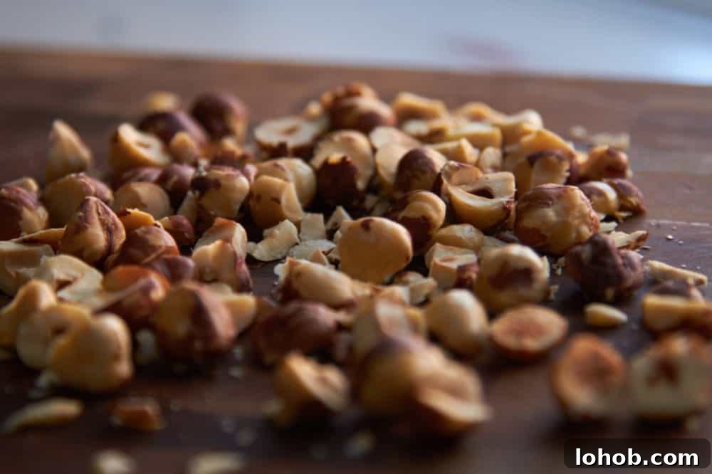 Crunchy Candied Hazelnuts Recipe for Snacks & Gifts 4 Chopped roasted hazelnuts on a wooden cutting board.