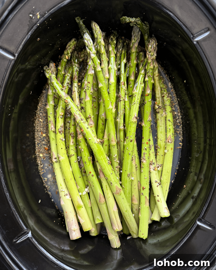 overhead shot of uncooked close up shot of Slow Cooker Lemon Garlic Asparagus in a black slow cooker