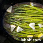 close up shot of Slow Cooker Lemon Garlic Asparagus in a black slow cooker, garnished with chopped lemon