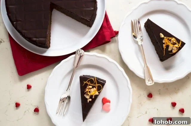 Flourless Chocolate and Hazelnut Torte Recipe 2 overhead of sliced chocolate hazelnut torte on white plates, next to a partially cut whole torte on a platter. Heart candies are sprinkled around the sliced torte and marble backdrop.