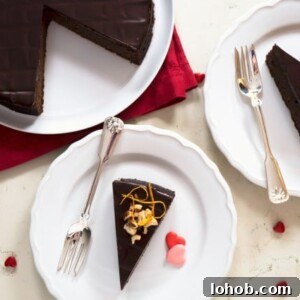 Flourless Chocolate and Hazelnut Torte Recipe 3 overhead of sliced chocolate hazelnut torte on white plates, next to a partially cut whole torte on a platter. Heart candies are sprinkled around the sliced torte and marble backdrop.