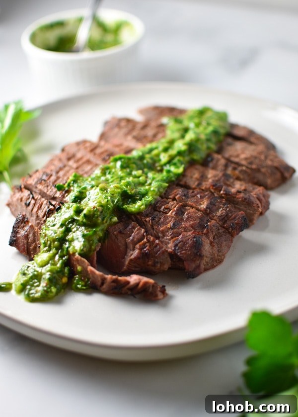 Grilled Flank Steak with zesty Chimichurri Sauce 4 Flank steak sliced on a grey plate with green chimichurri sauce drizzled on top