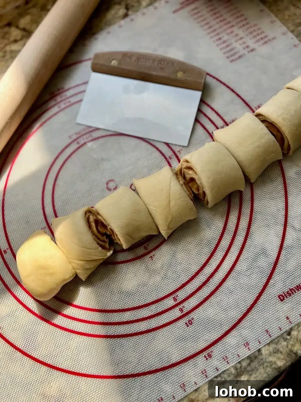Soft Gooey Cinnamon Rolls Recipe for Perfectly Fluffy Layers 11 The log of cinnamon roll dough has been cut into even pieces and sits next to a bench knife and a rolling pin.