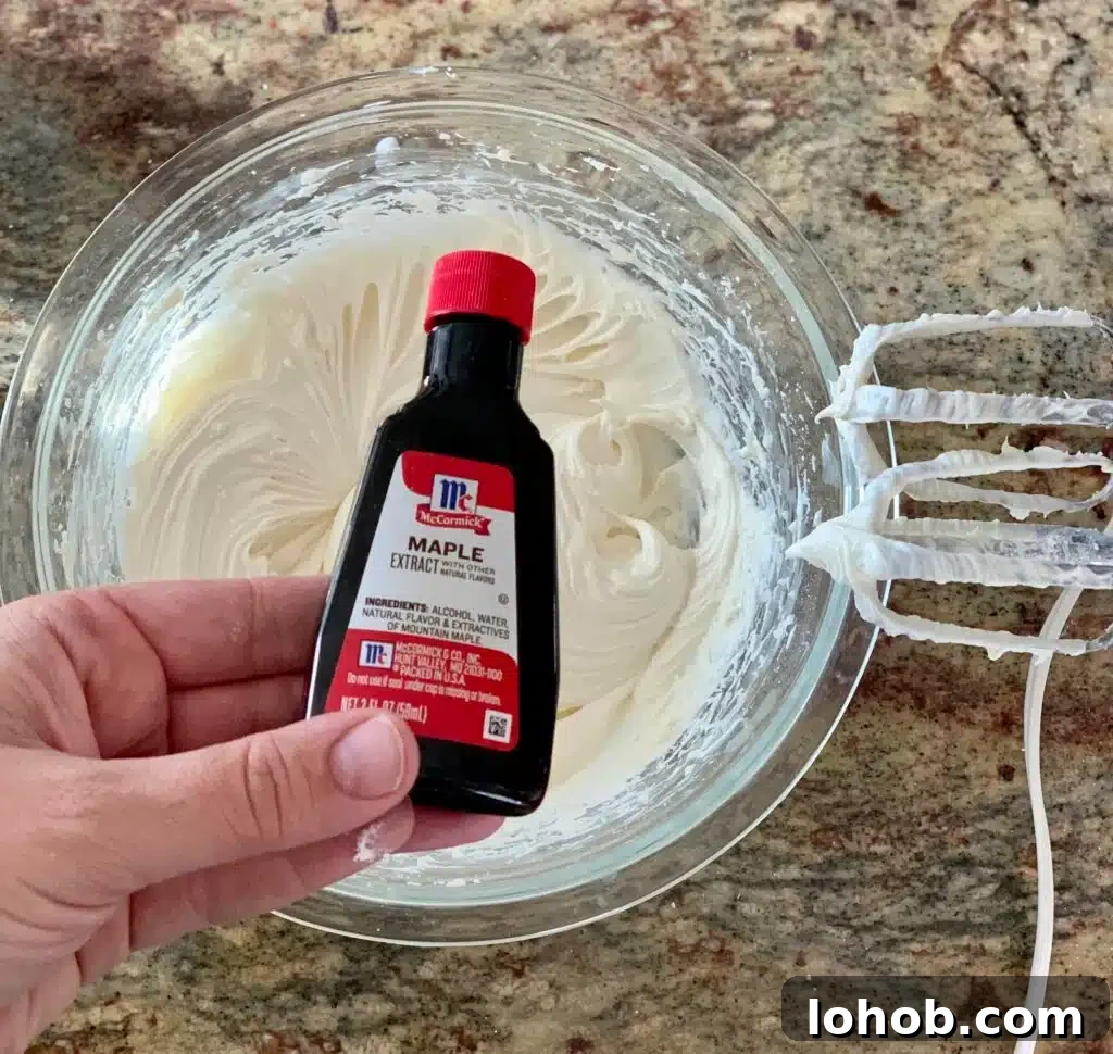 Soft Gooey Cinnamon Rolls Recipe for Perfectly Fluffy Layers 15 Maple extract is held over a mixing bowl of frosting.