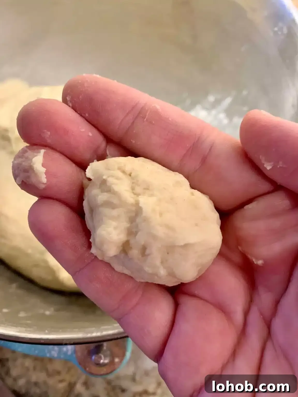 Soft Gooey Cinnamon Rolls Recipe for Perfectly Fluffy Layers 7 A hand holds a small ball of dough that is the right consistency (not overly sticky) over a stand mixer.