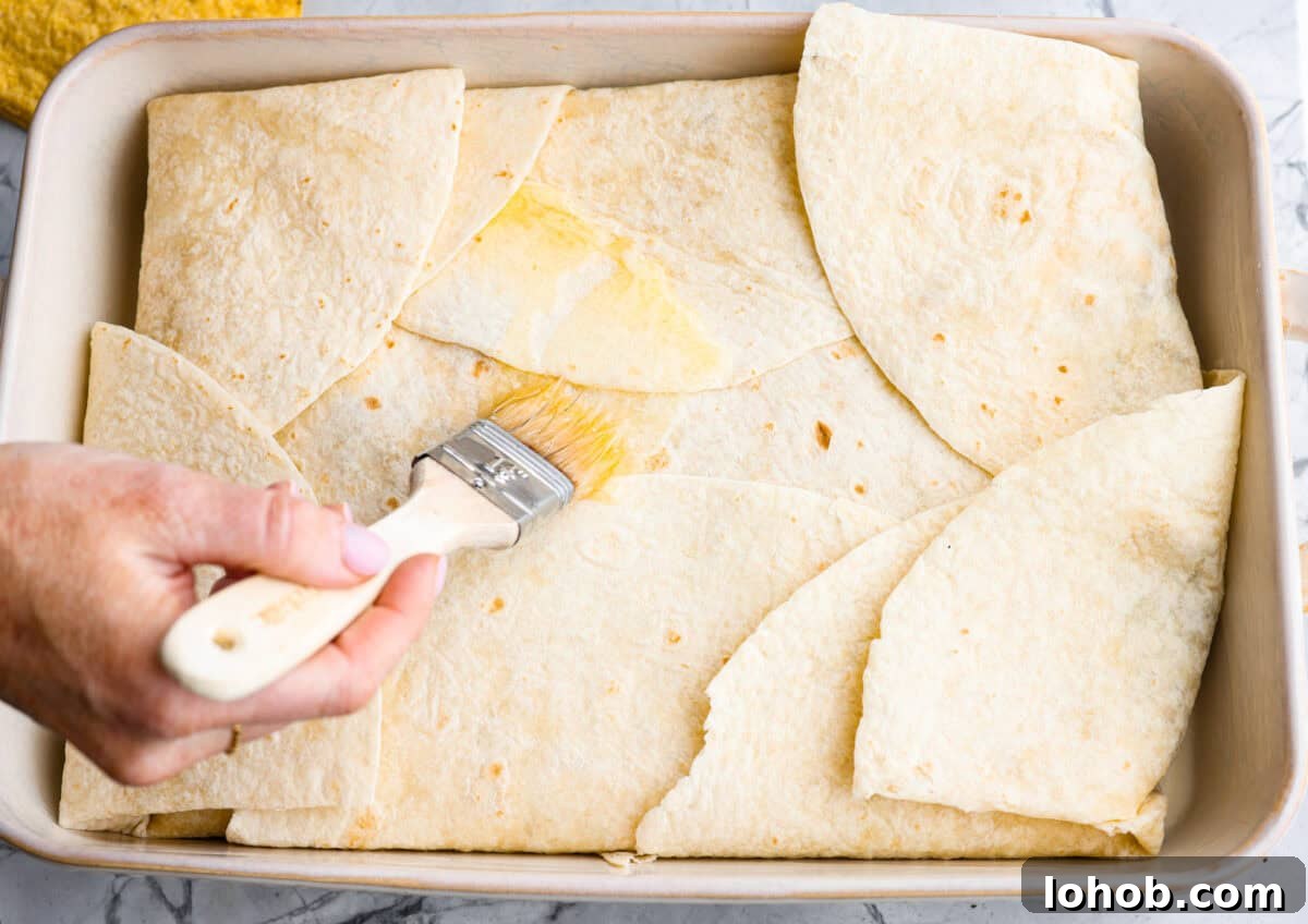 Tortillas folded in over the layers and someone is spreading butter on the the crunchwrap casserole.