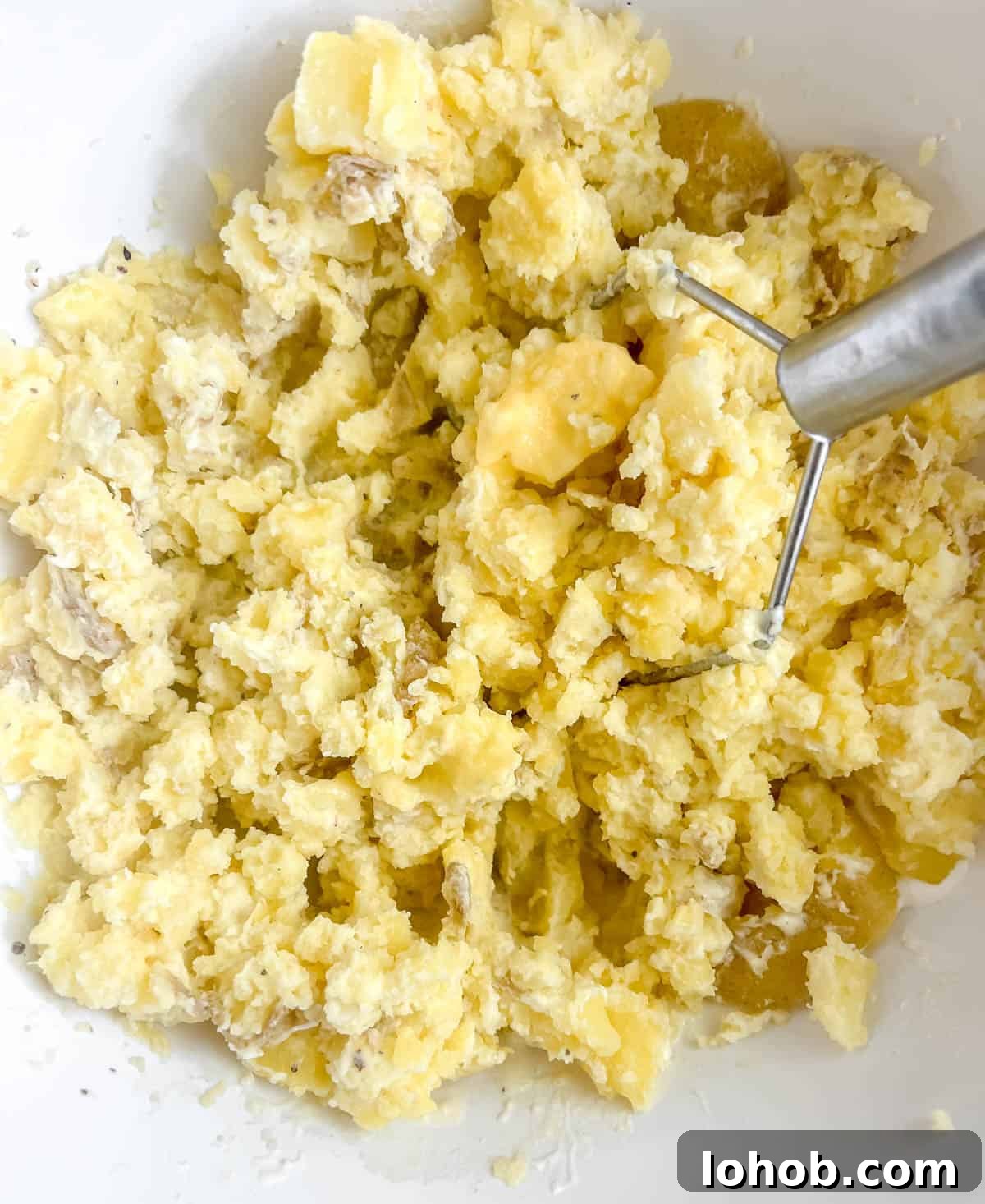 Mashed potatoes with greek yogurt in a bowl with a potato masher.