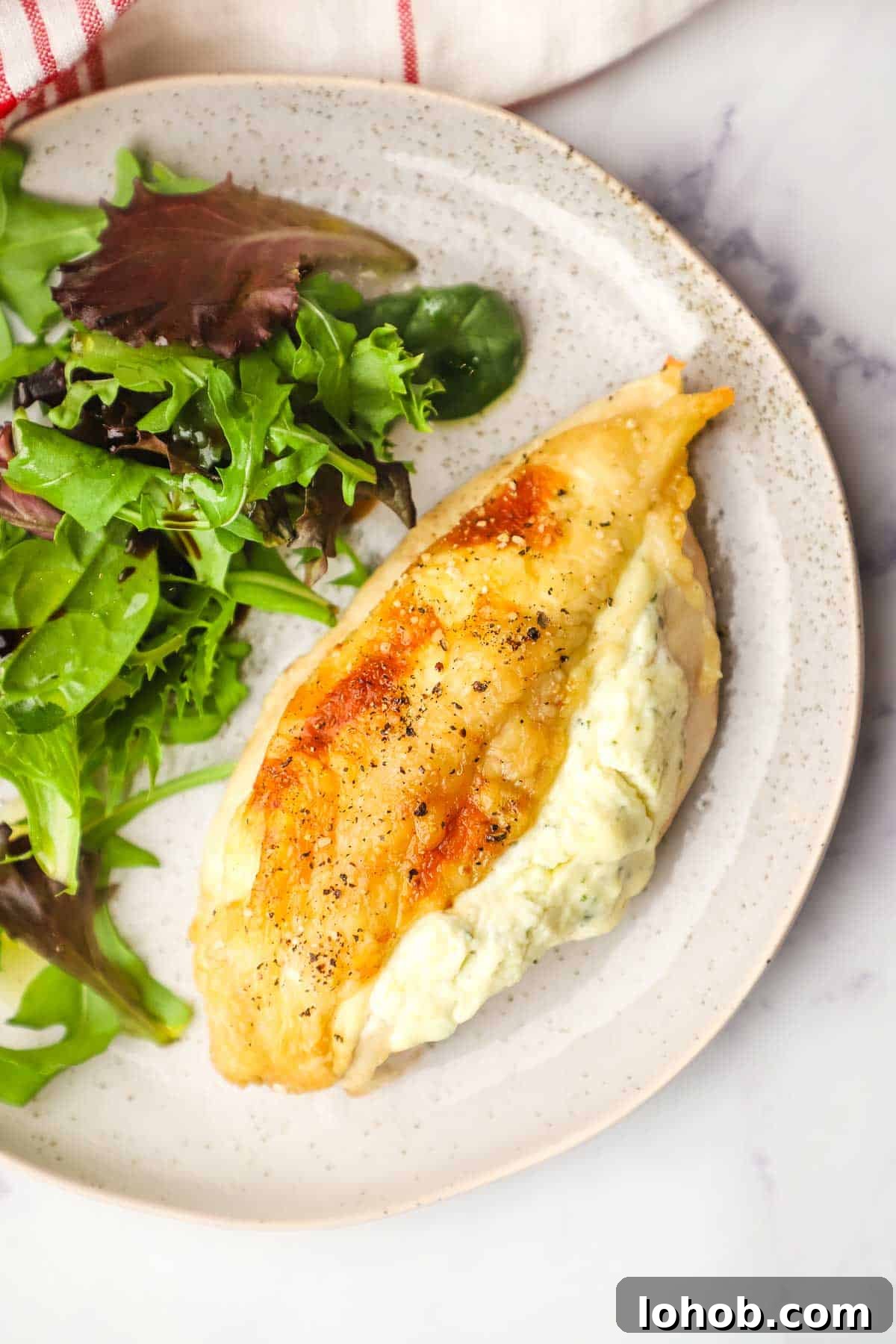 Creamy Boursin-Stuffed Chicken Breast Recipe 10 Overhead view of a Boursin-Stuffed Chicken breast on a plate with salad on the side.