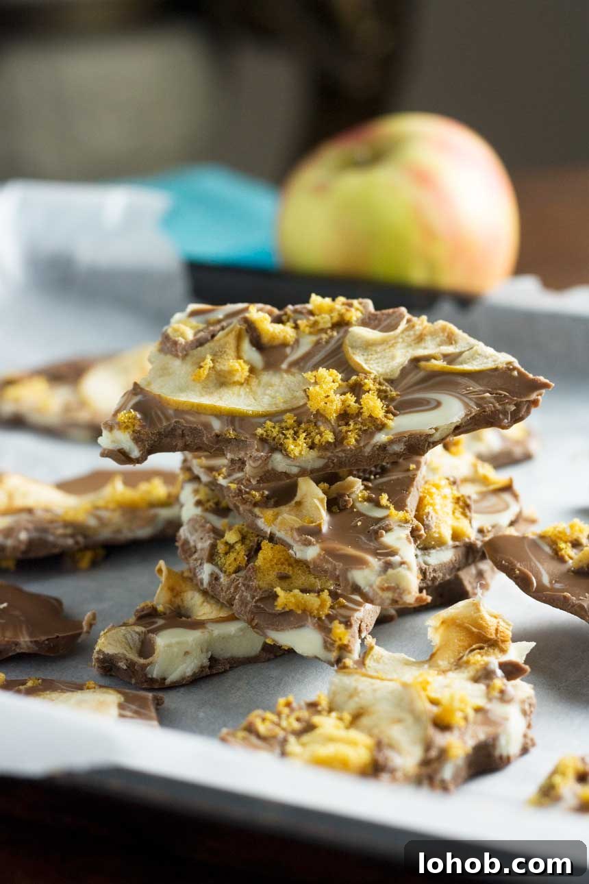 A closeup of a stack of toffee apple chocolate bark on baking paper with an apple in the background.