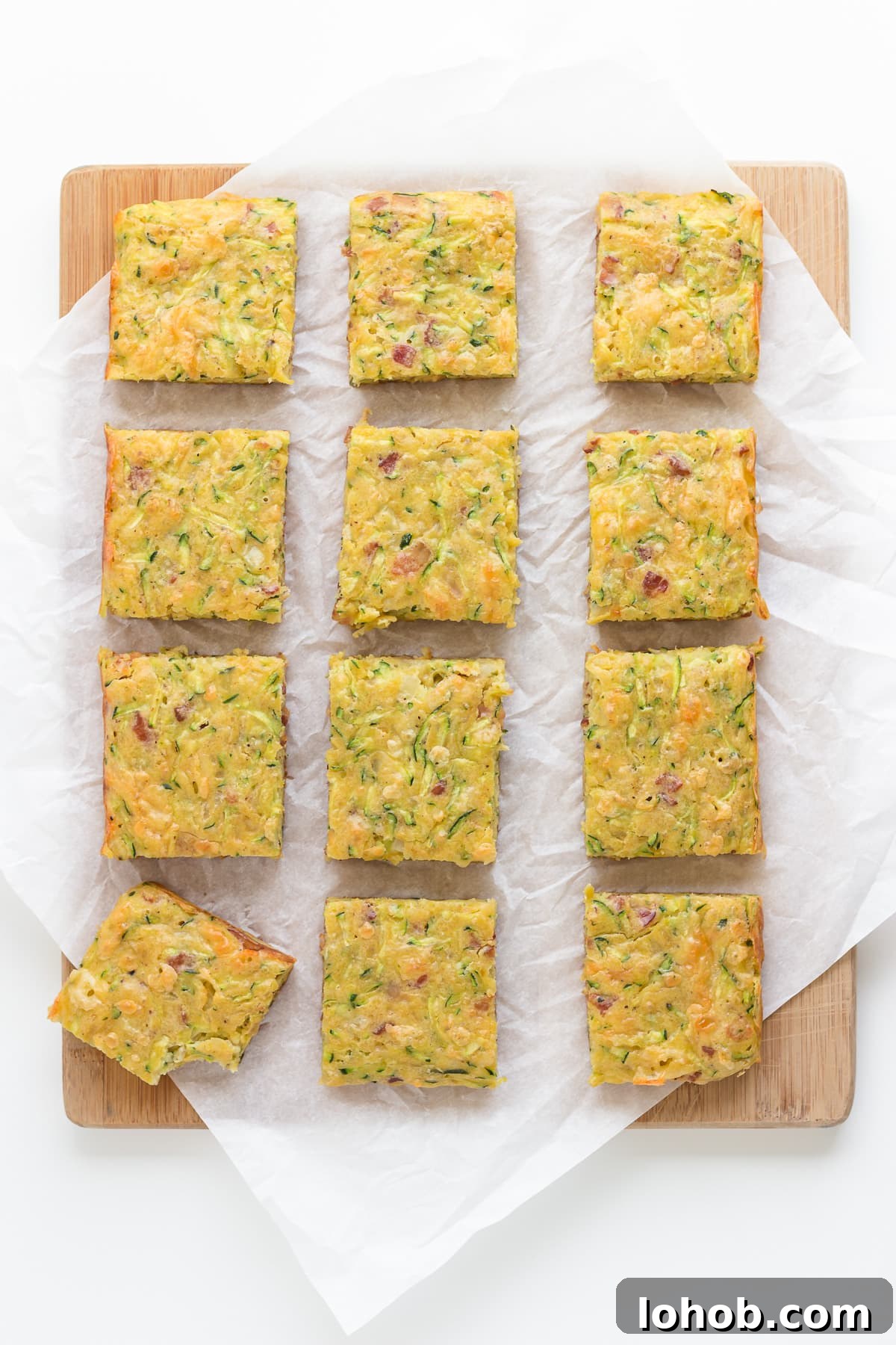 Square cut up pieces of zucchini slice on a wooden board lined with parchment paper.