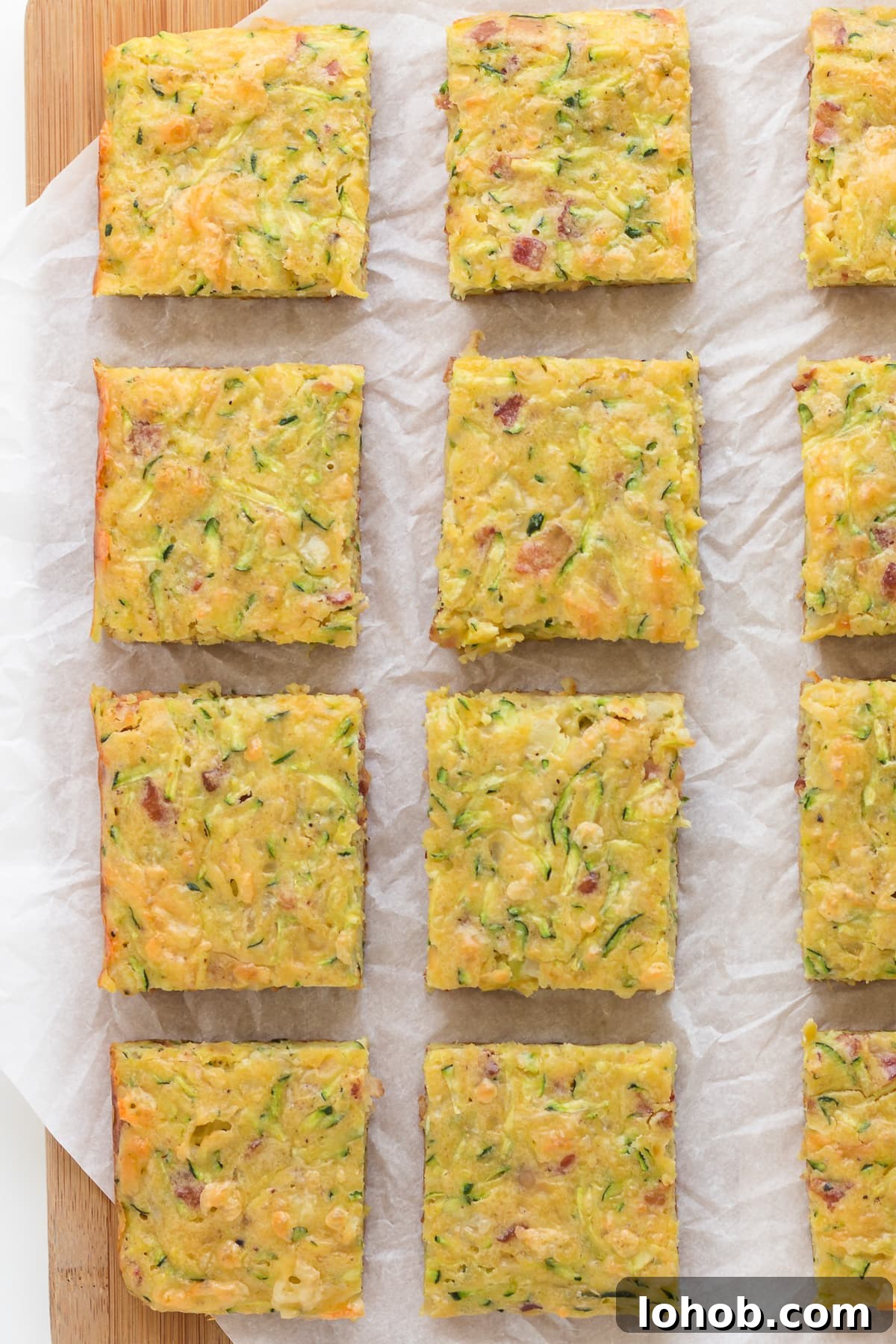 Closeup of square pieces of zucchini slice on a wood board lined with a piece of parchment paper.