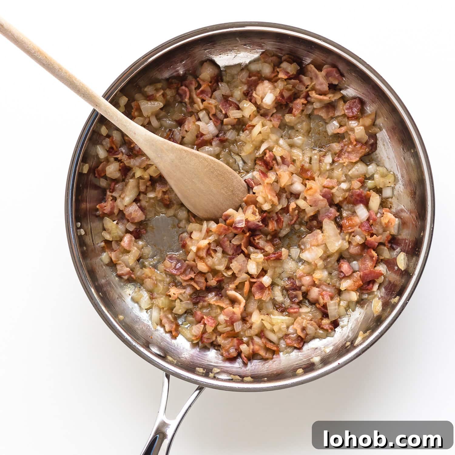 Sautéed bacon and onions in a stainless steel frying pan.