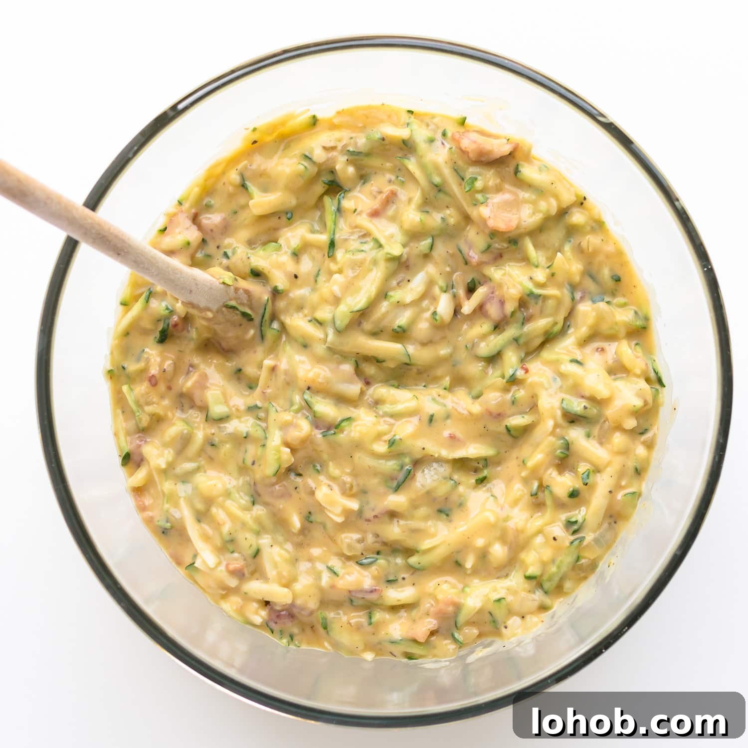 Zucchini slice batter in a glass mixing bowl with wooden spoon.
