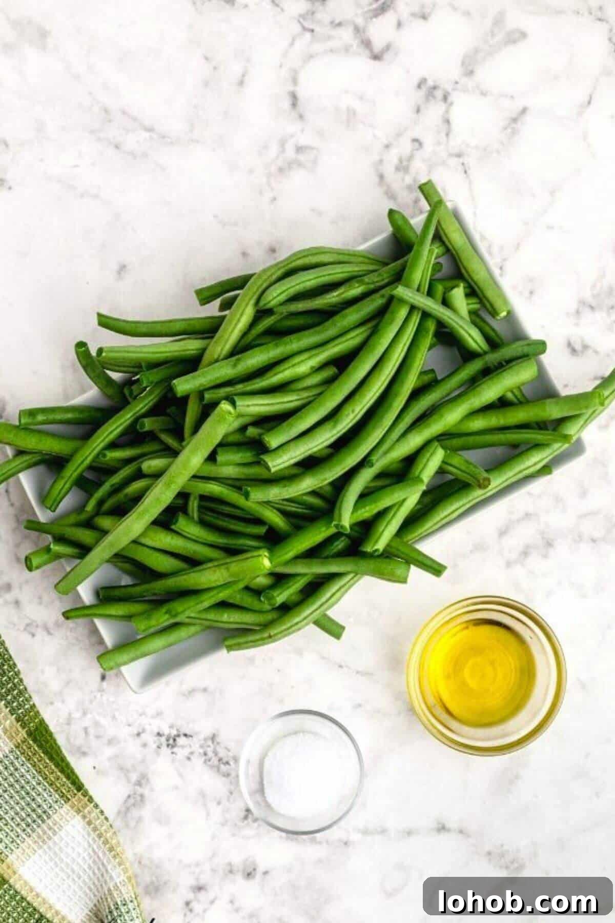 Crispy Air Fryer Green Beans with Garlic and Parmesan 4 Uncooked green beans, olive oil and seasonings measured on a white marble table.