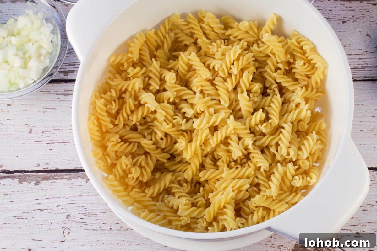 Leftover Ham and Pea Pasta Recipe for Quick Weeknight Meals 4 Drained pasta in colander on faux wood surface.