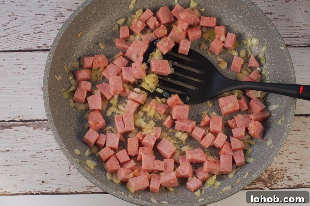 Leftover Ham and Pea Pasta Recipe for Quick Weeknight Meals 5 Cubed ham and onions in skillet with black spatula.