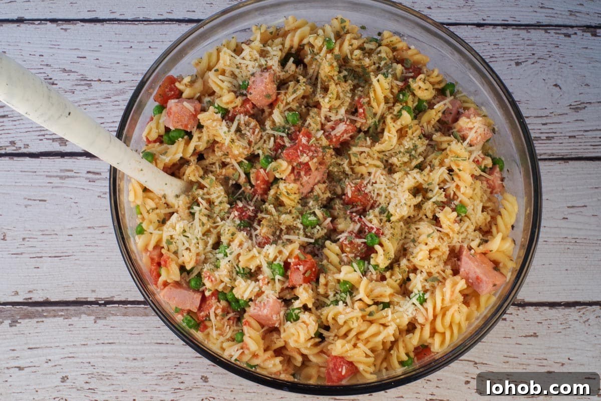 Leftover Ham and Pea Pasta Recipe for Quick Weeknight Meals 10 Pasta mixed with ham mixture in large glass bowl with spoon.