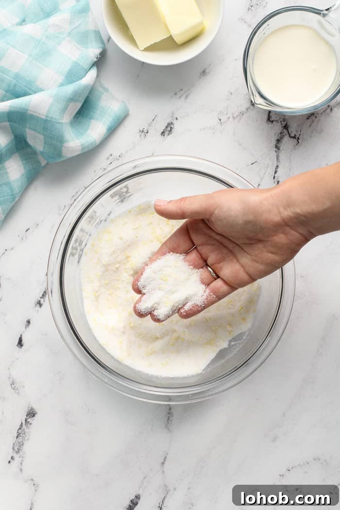Hand showing sugar and lemon zest rubbed together in a glass mixing bowl