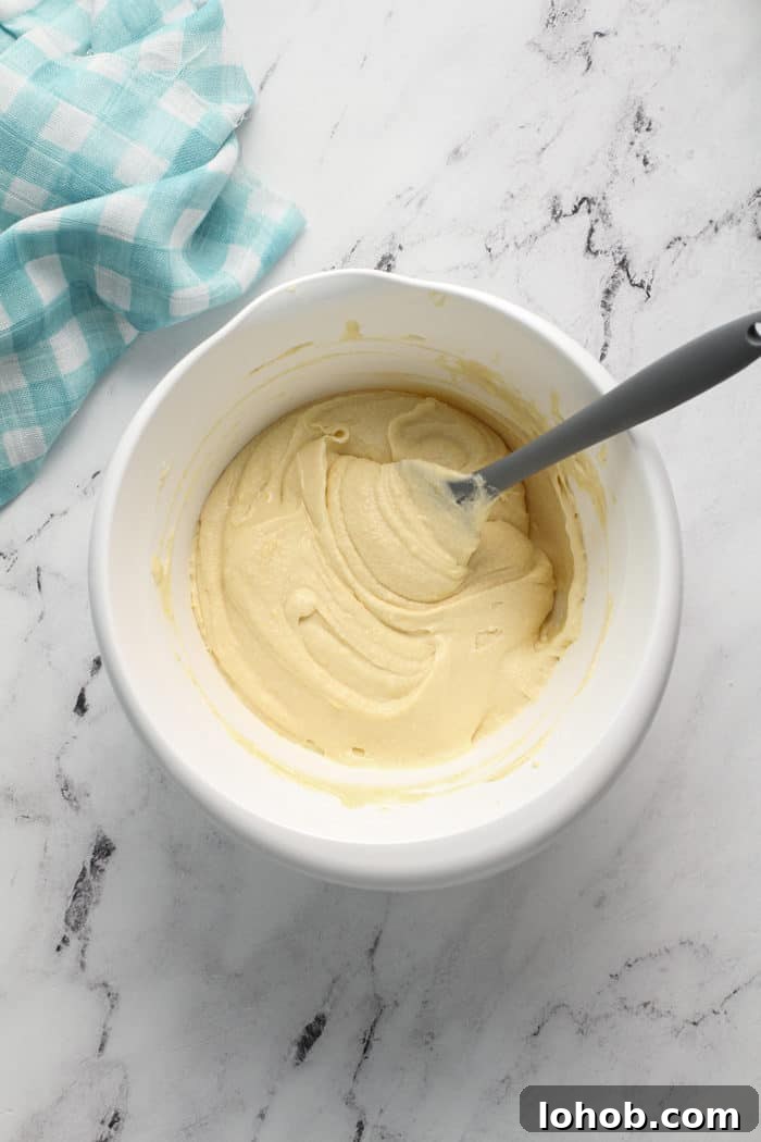 Spatula folding together lemon whipping cream cake batter in a white mixing bowl