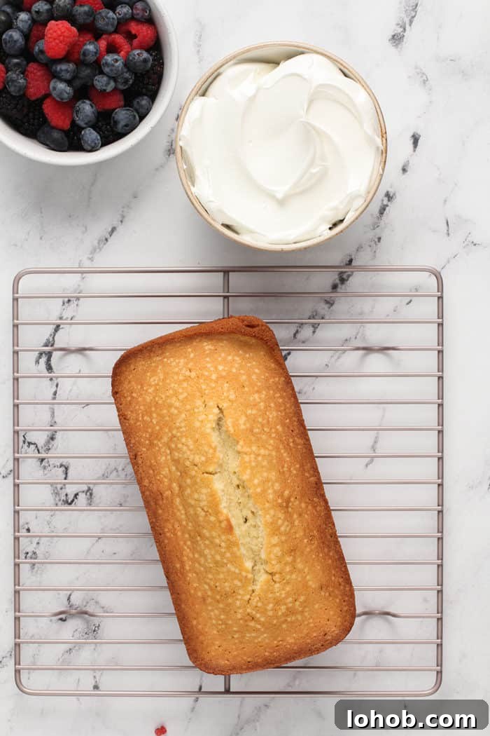 Overhead view of lemon whipping cream cake cooling on a wire rack next to a bowl of whipped cream and fresh berries