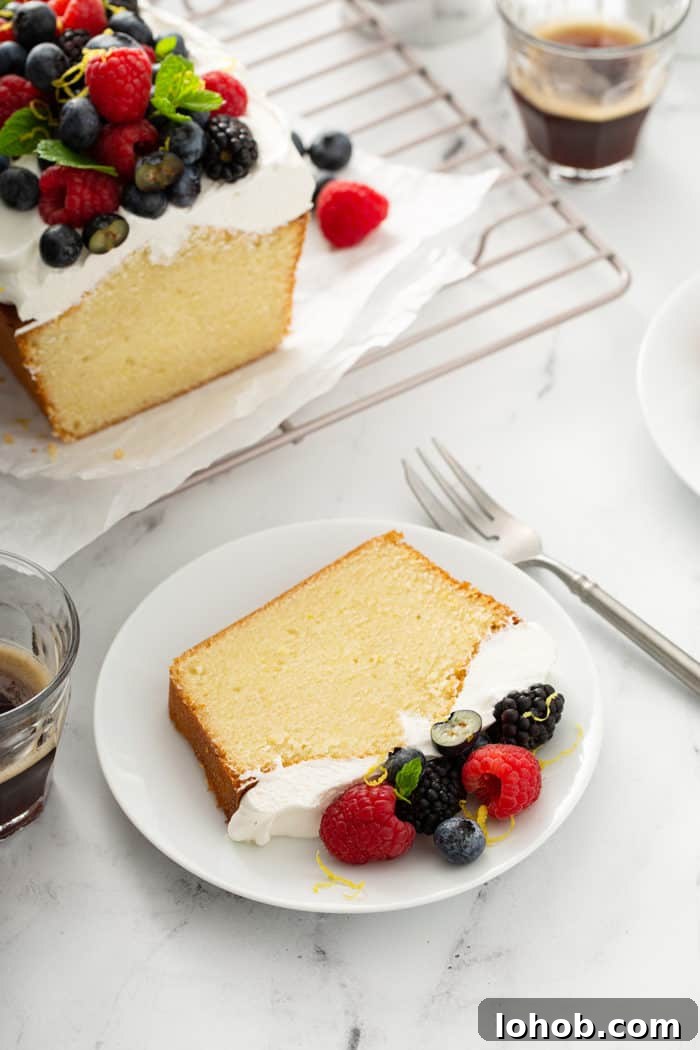 Slice of lemon whipping cream cake on a white plate, with a fork and more cake on the counter next to it