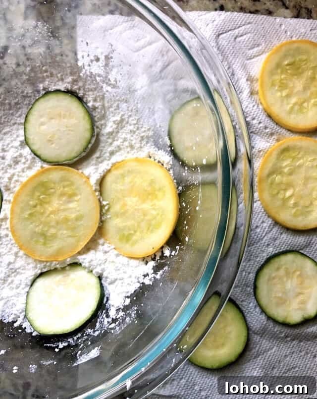Crispy Fried Zucchini Chips Recipe for Perfect Snack 4 zucchini chips dredged in cornstarch in a bowl.