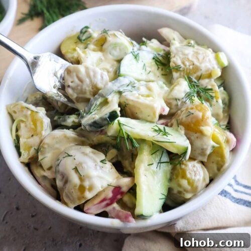 glass bowl with potato salad and cucumbers topped with fresh dill.
