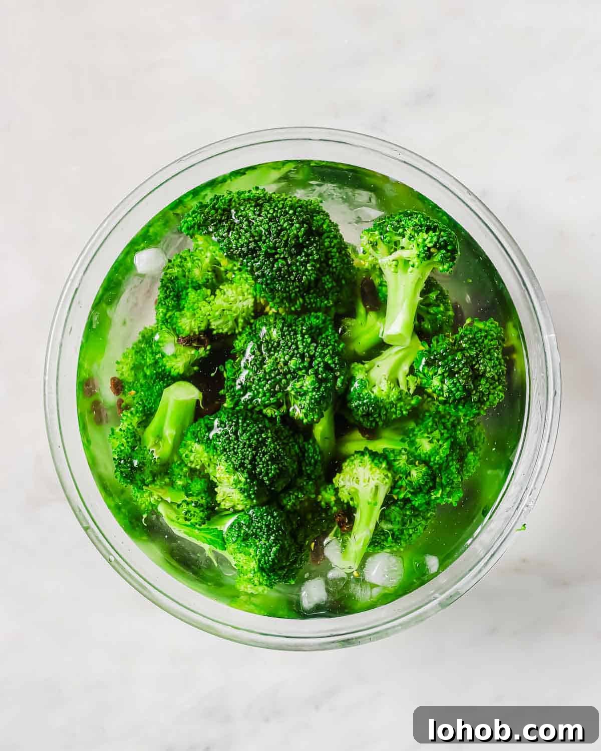 A bowl filled with bright green broccoli florets and raisins immersed in ice water.