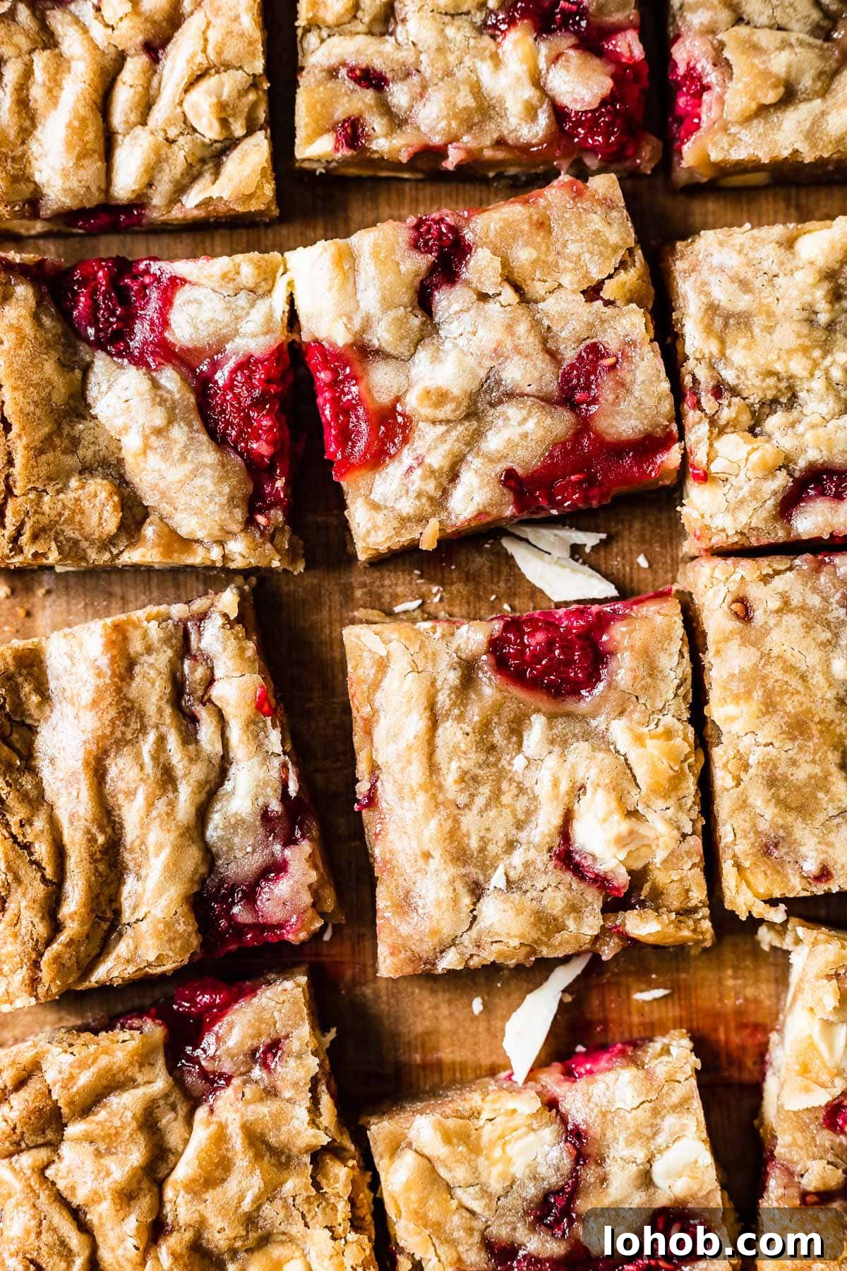 Raspberry White Chocolate Blondies Recipe — Chewy, Fruity Bars 2 Squares of blondies studded with raspberries and white chocolate on a wooden cutting board.