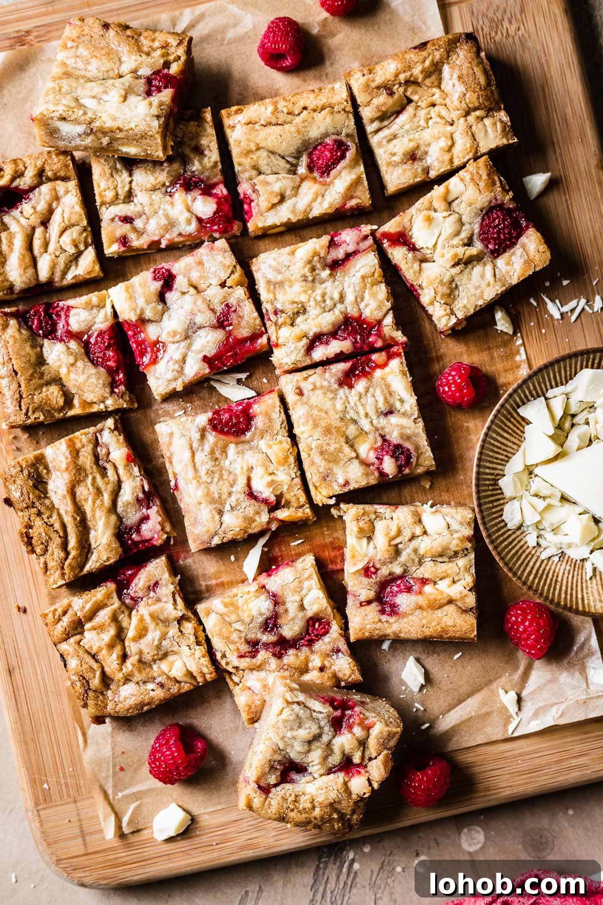 Raspberry White Chocolate Blondies Recipe — Chewy, Fruity Bars 12 Raspberry white chocolate blondie squares on a wooden cutting board.